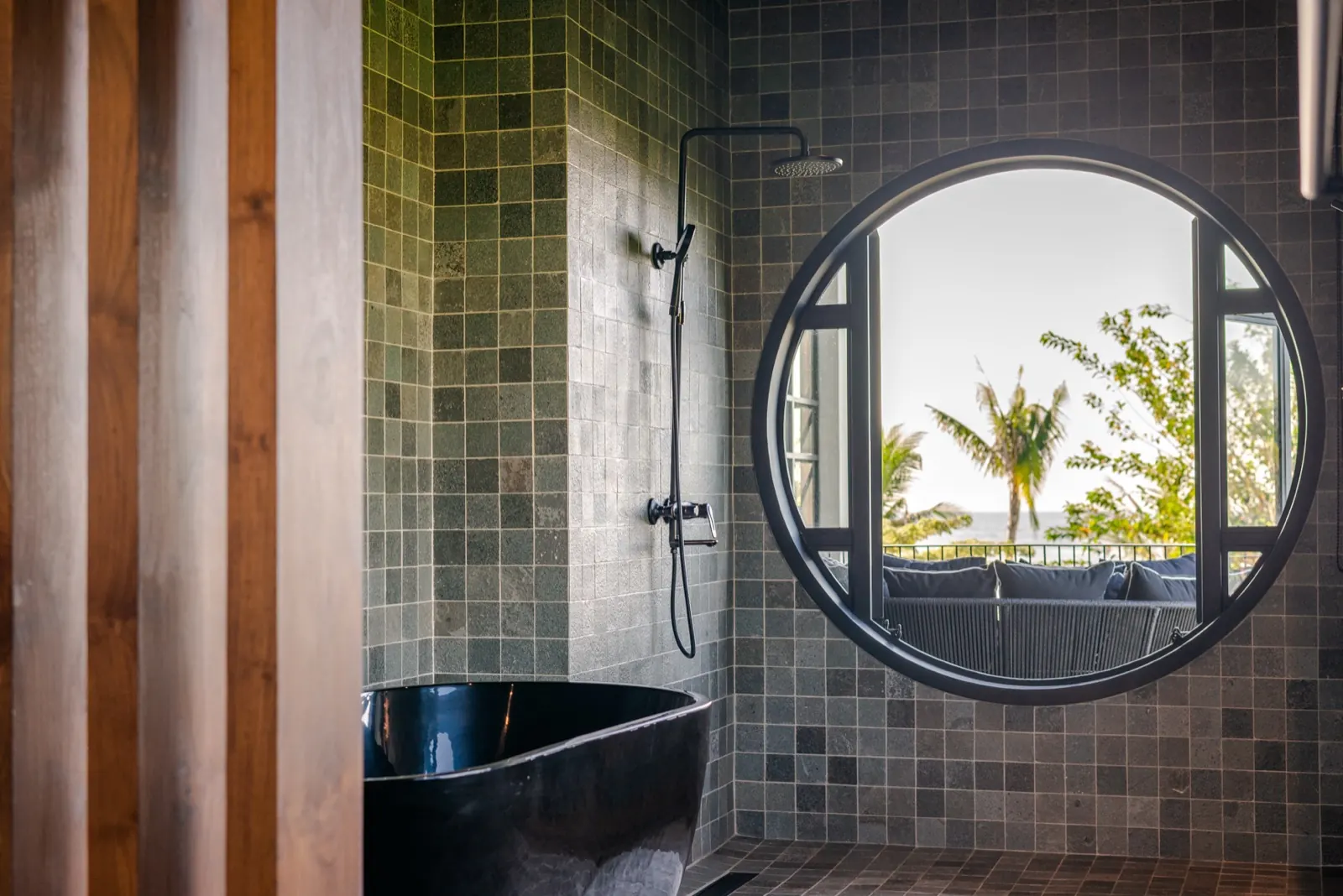The black stone tub under a round window, palms and sea beyond