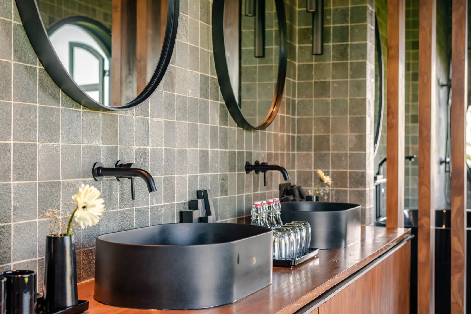 Twin black basins on teak, round mirrors on green tile