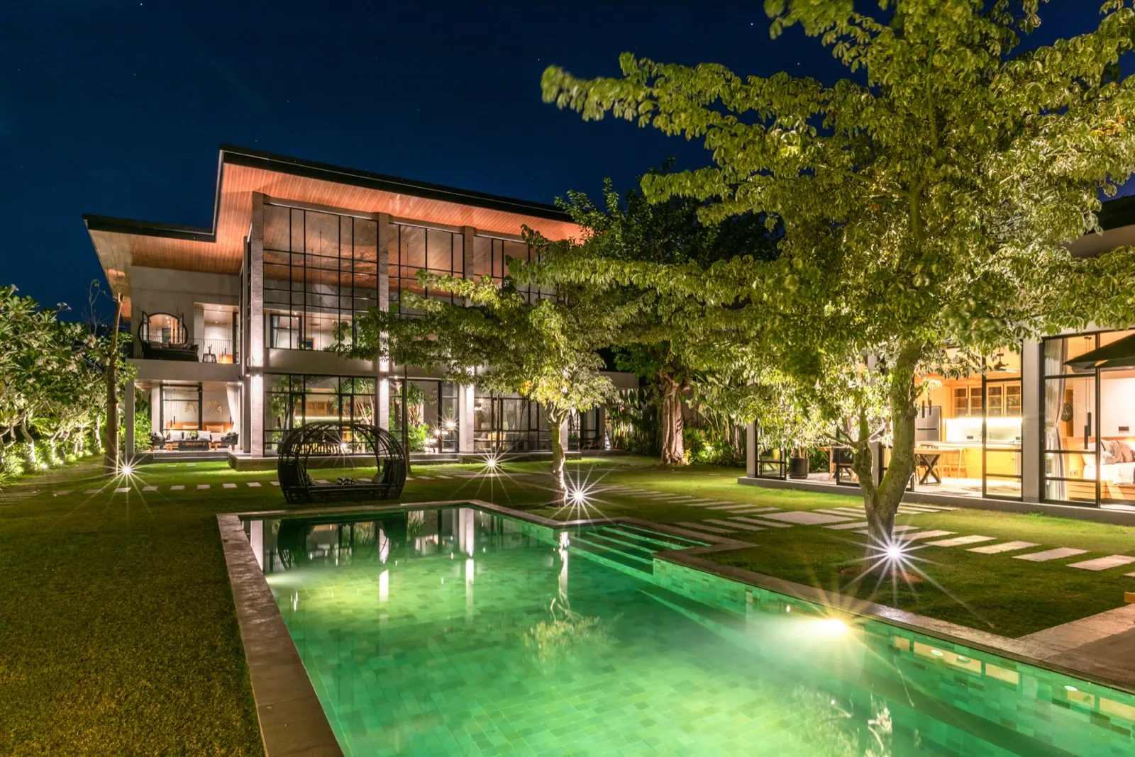 The pool house at night, the pool glowing under the trees