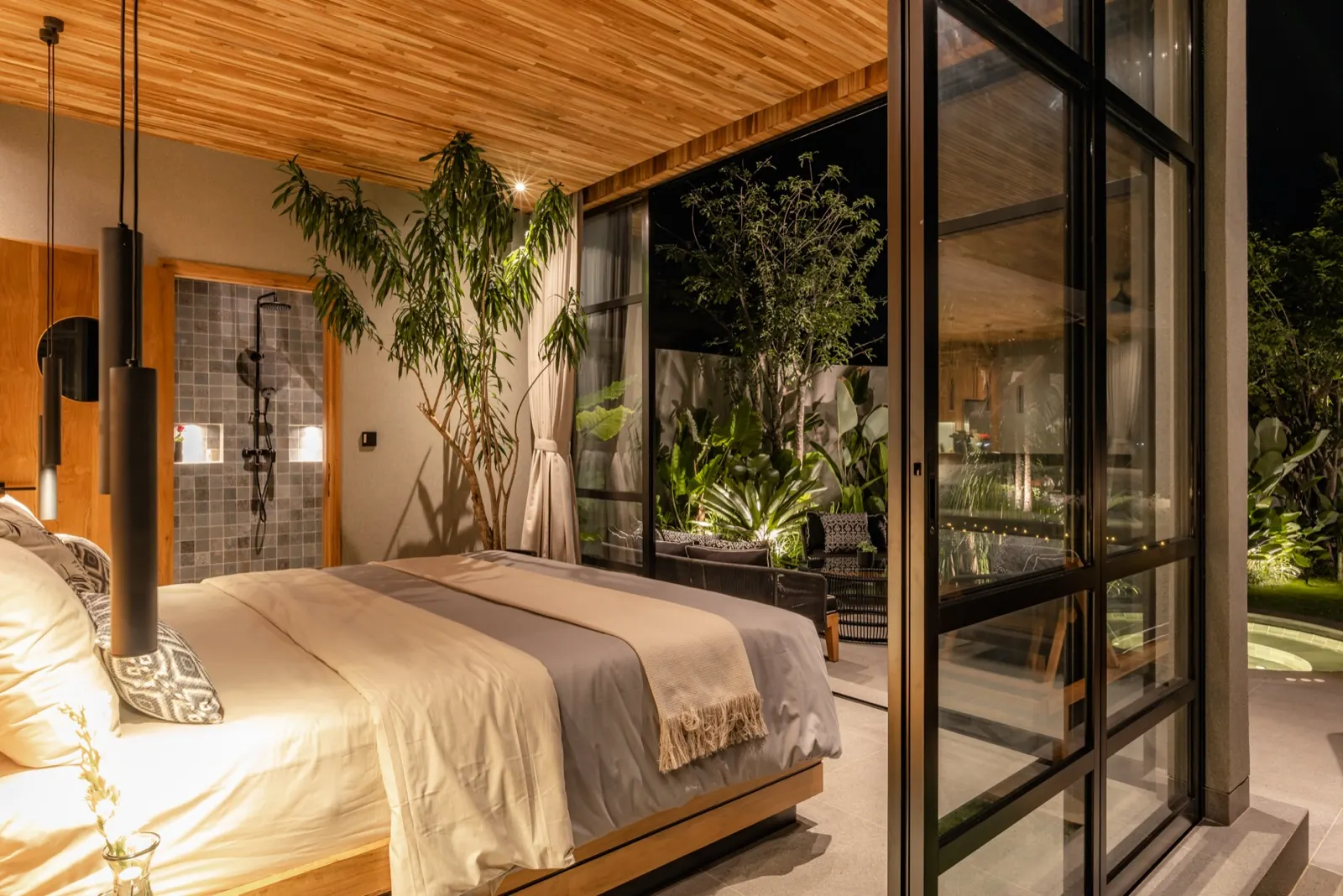 A queen suite at night, timber ceiling, garden beyond the glass